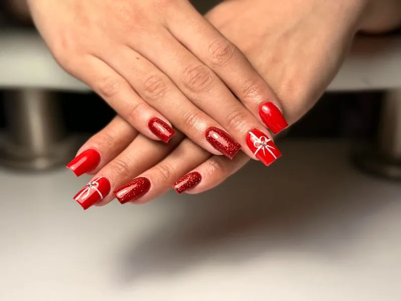 Karácsonyi gél lakk manikűr: piros csillámmal és kézzel festett fehér masni díszítéssel - Minimal Nails Mosonmagyaróvár